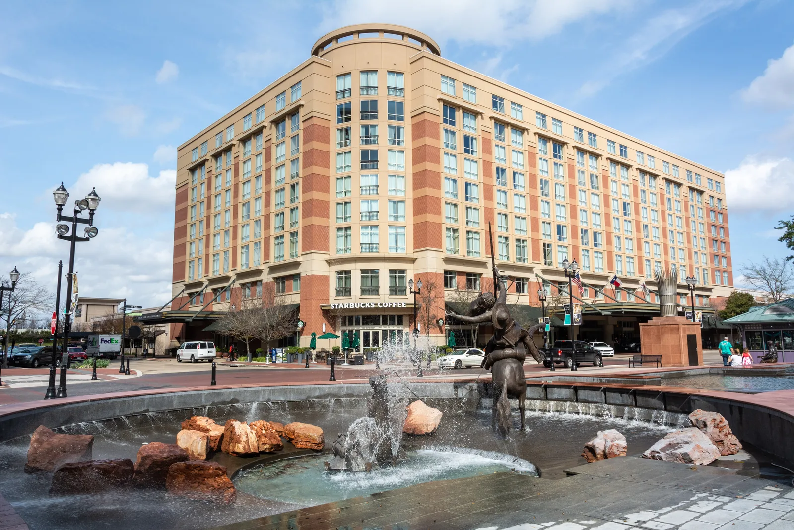 Brick and stone hotel building above a town-square fountain with a bronze sculpture and red boulders