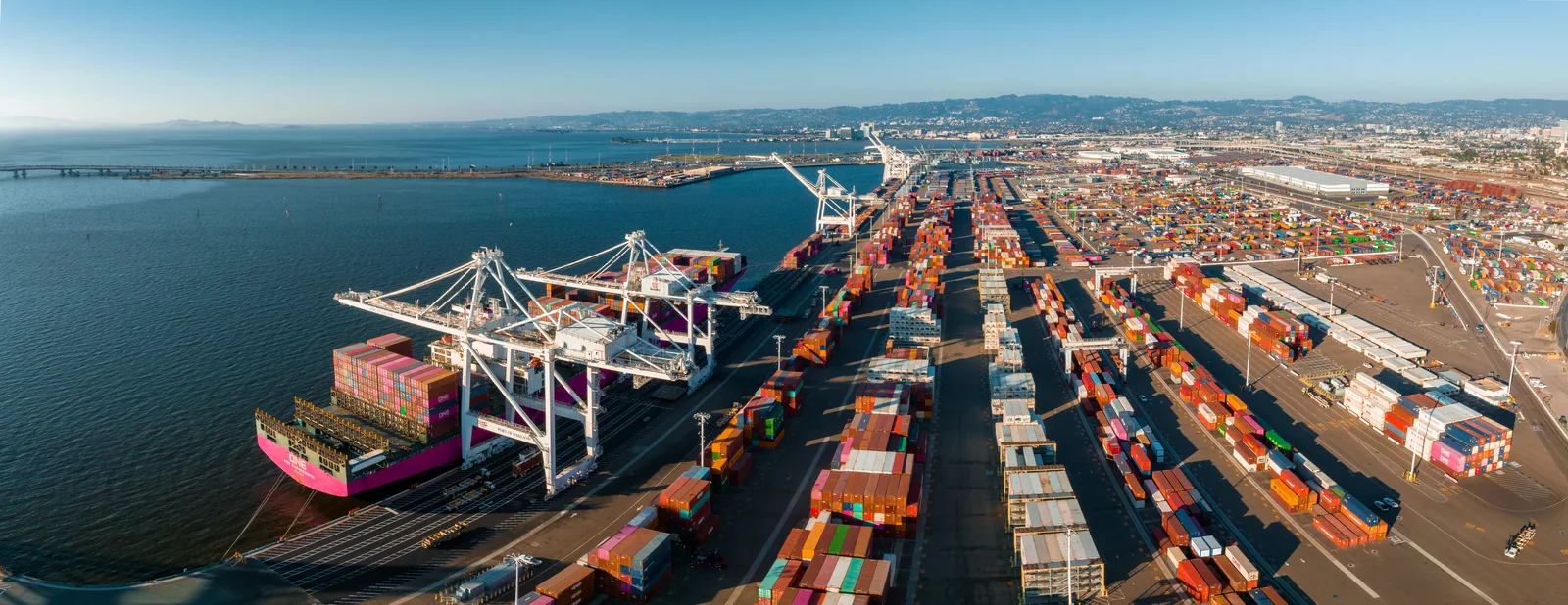 Aerial view of a container port with ship-to-shore cranes unloading a vessel beside stacked containers