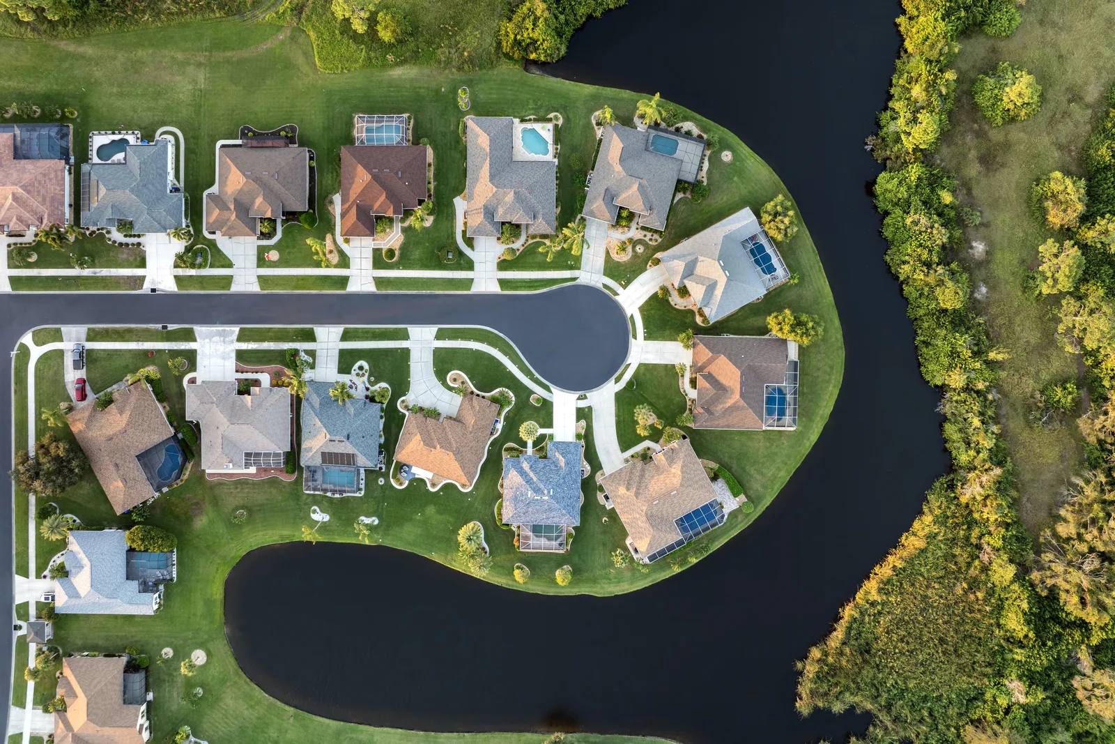 Overhead aerial view of a cul-de-sac of houses with pools and screened lanais beside a winding canal