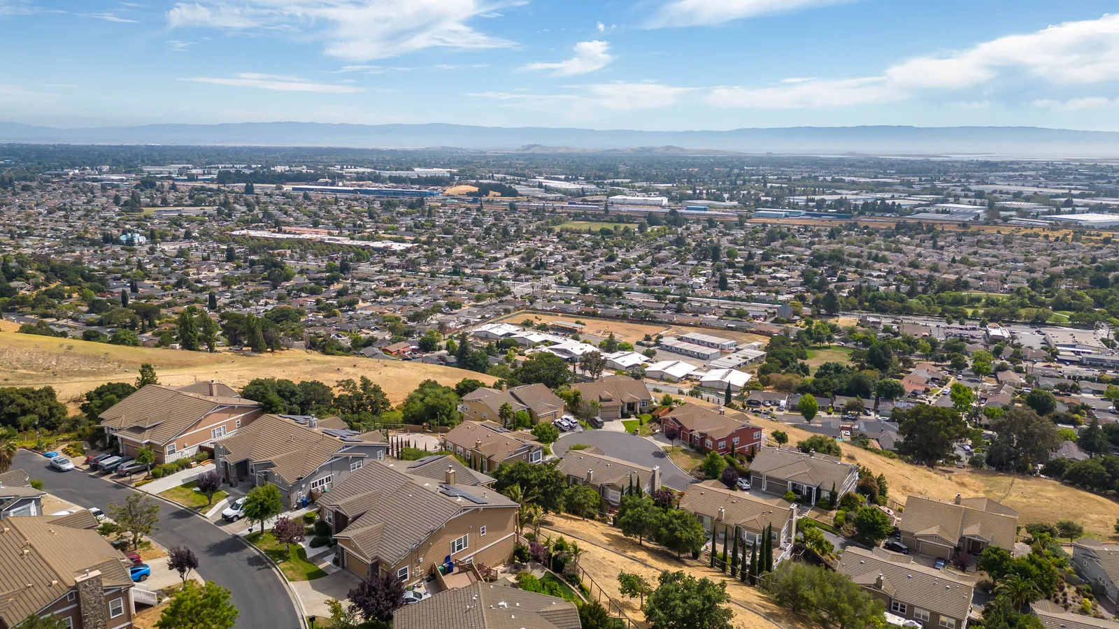 Aerial view from a dry hillside over a housing tract and a dense suburban grid stretching to distant hills