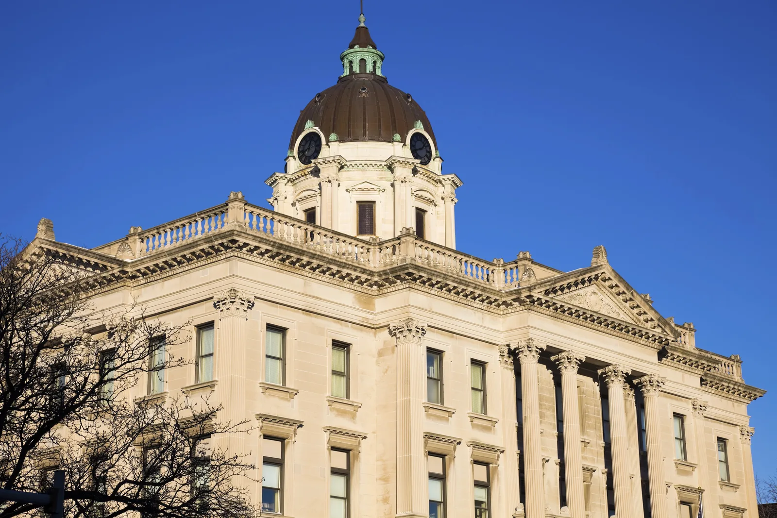 Neoclassical limestone civic building with Corinthian columns and a copper-trimmed clock dome against blue sky