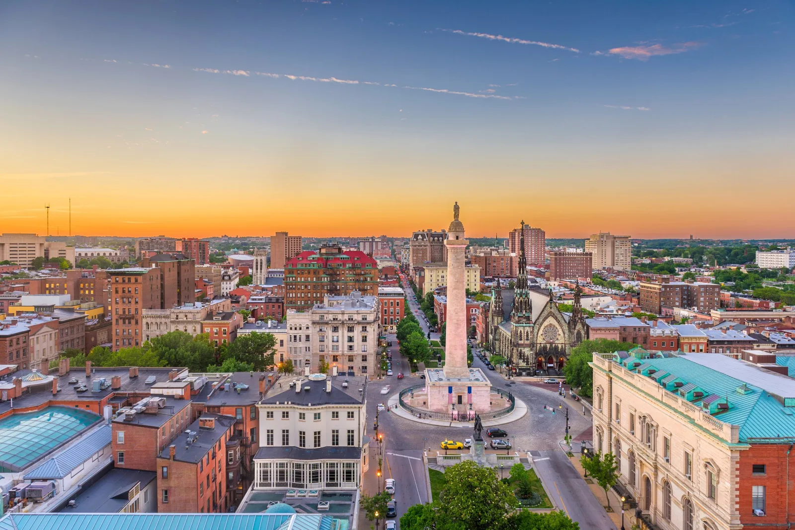 City skyline at sunset with a tall column monument in a circle, a Gothic church and brick buildings