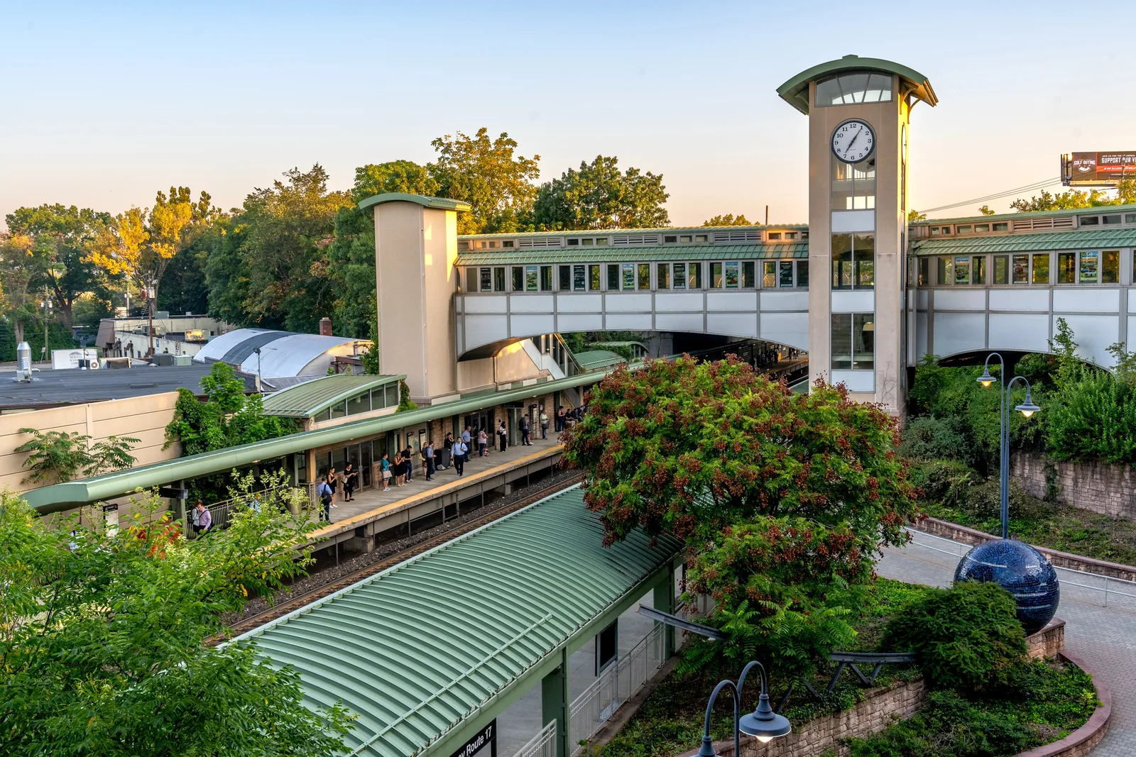 Commuter rail station with green-roofed platforms, a clock tower and an enclosed pedestrian bridge over the tracks