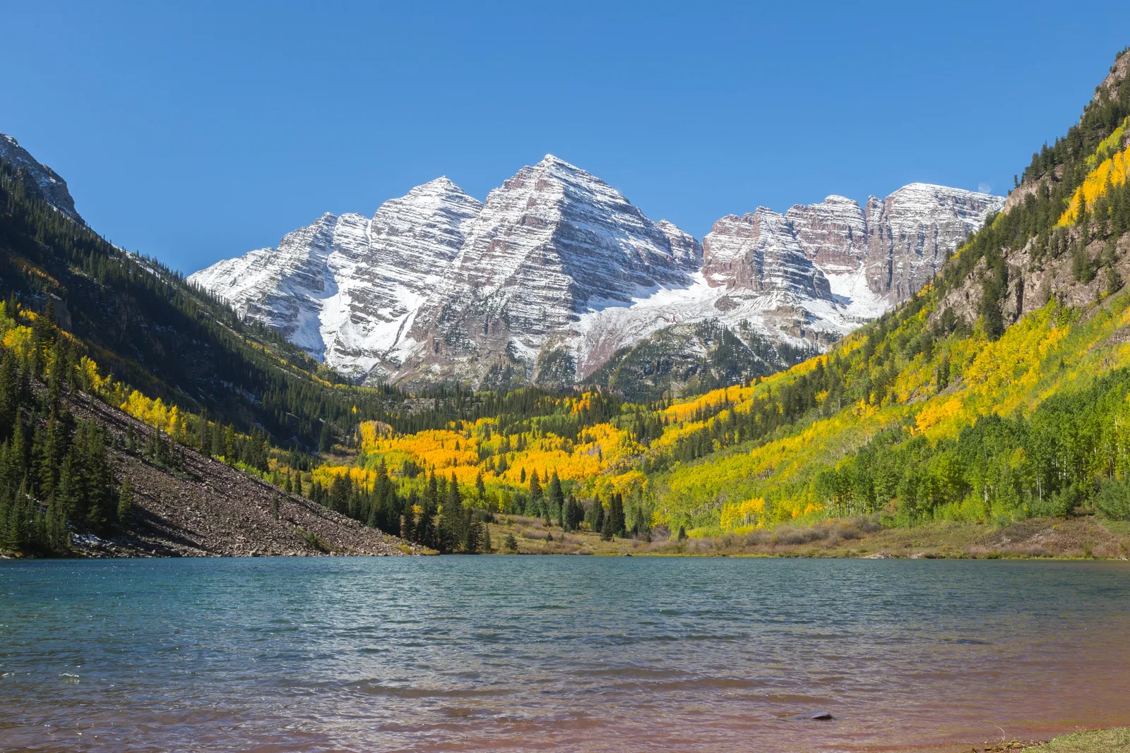 Snow-dusted rocky peaks above a mountain lake, with slopes of golden aspens and dark conifers