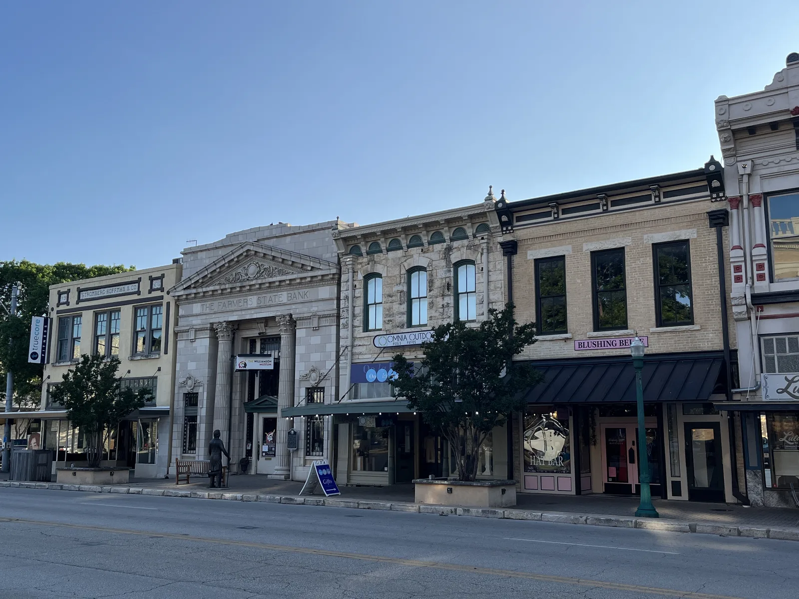 Row of historic two-storey stone and brick storefronts, including a columned former bank, along an empty street