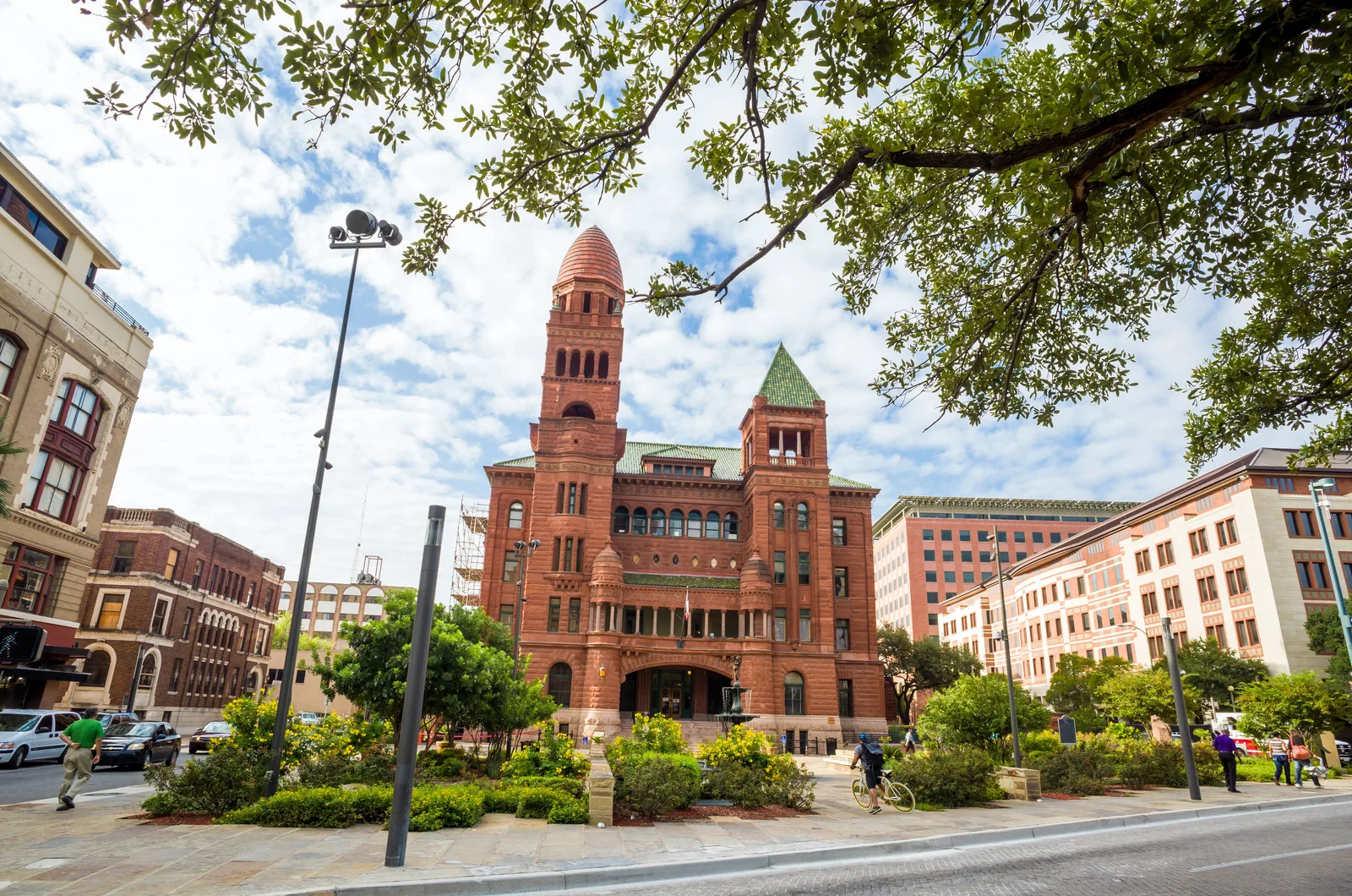 Red sandstone Romanesque-style civic building with a tall tower, framed by oak branches and city streets