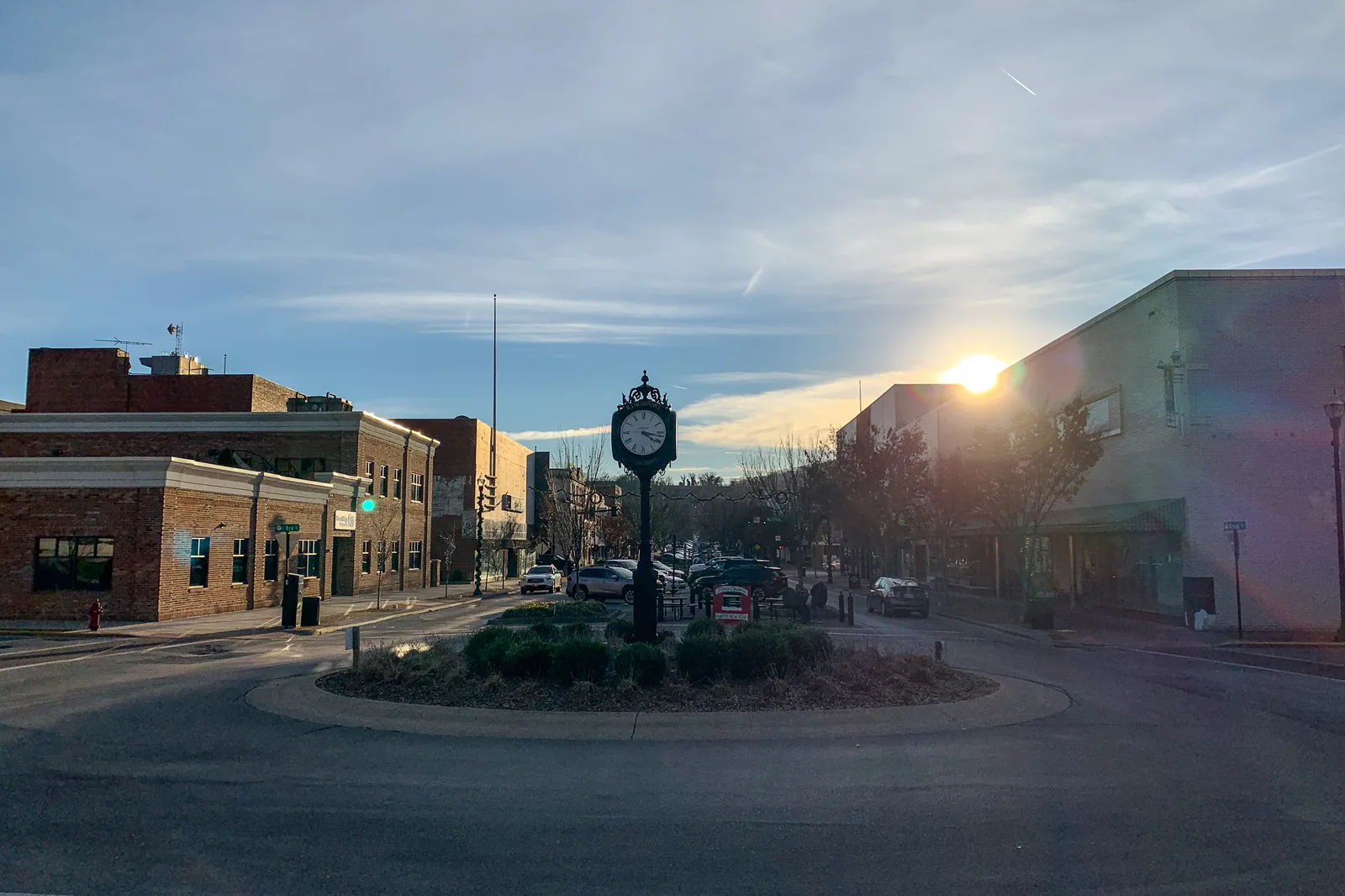 Downtown street with an ornate clock post in a landscaped roundabout, brick buildings and low winter sun