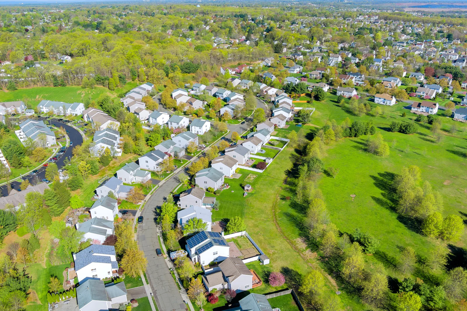 Aerial view of a suburban housing development with curving streets, rooftop solar panels and an open green field