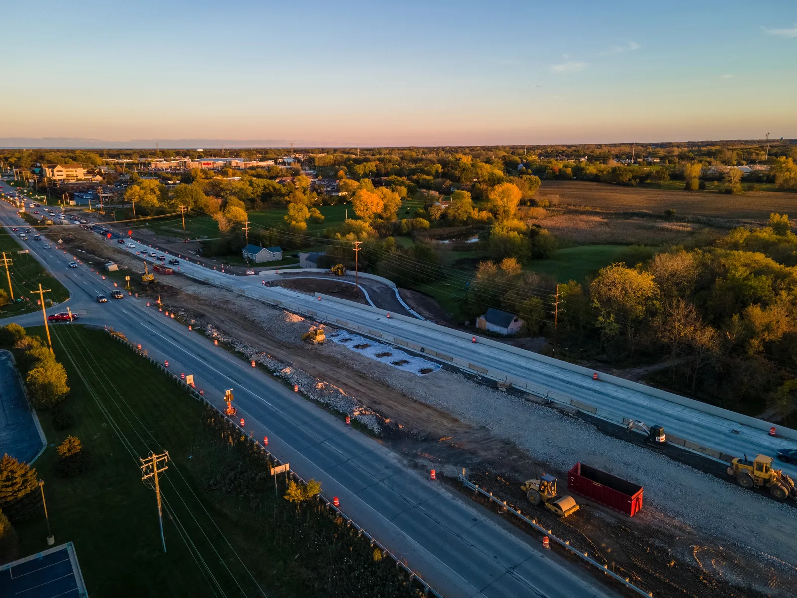 Aerial view of road widening at sunset, with traffic cones, a new concrete lane, a roller and loaders