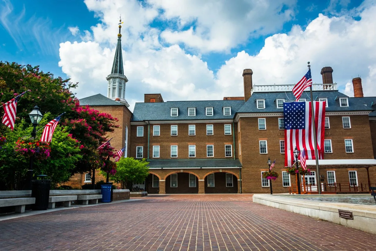 Brick civic building with a white steeple, American flags and a brick-paved plaza with fountain