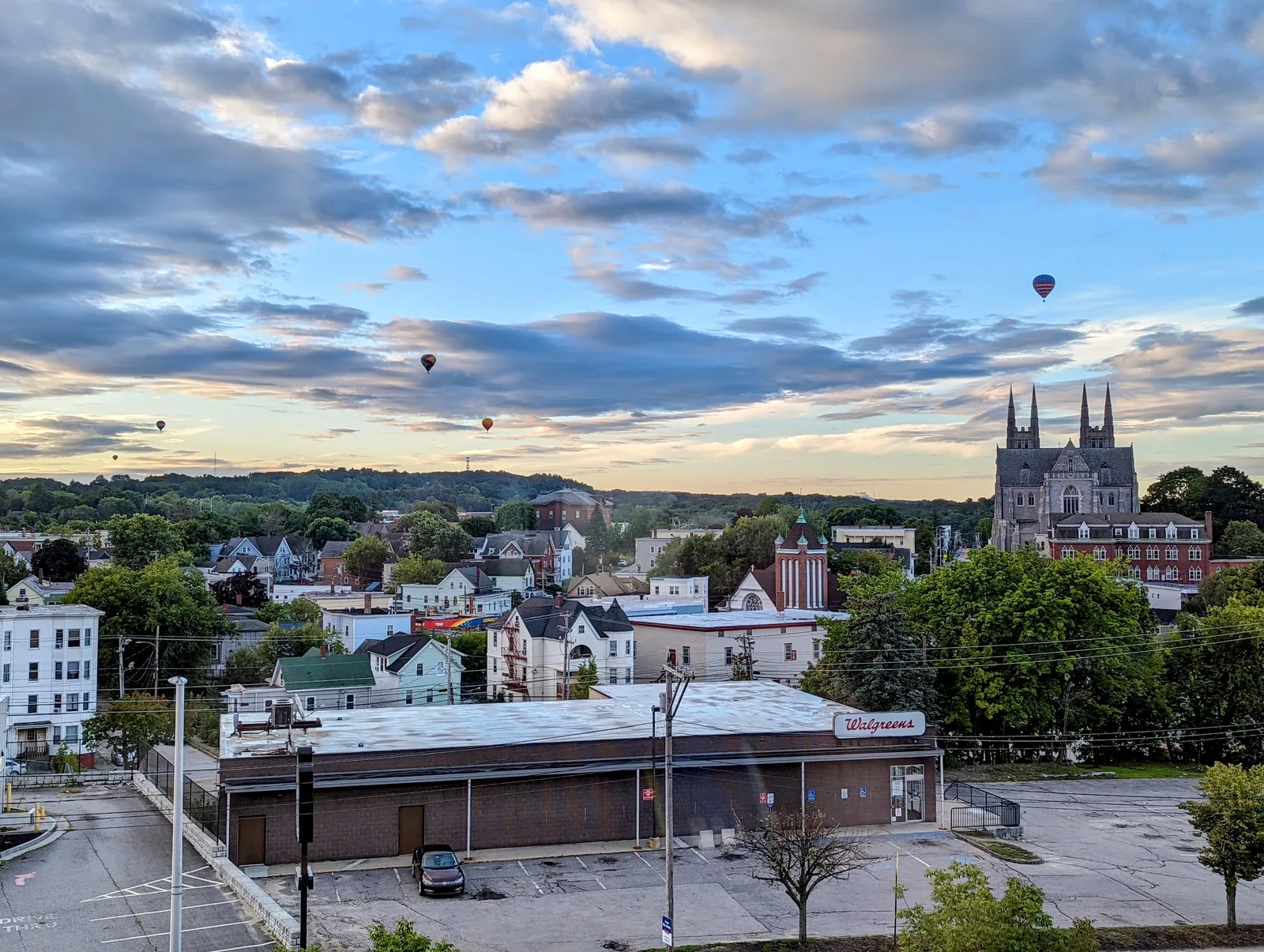 View over a small city of houses and a Gothic church with twin spires, hot-air balloons in a cloudy sky