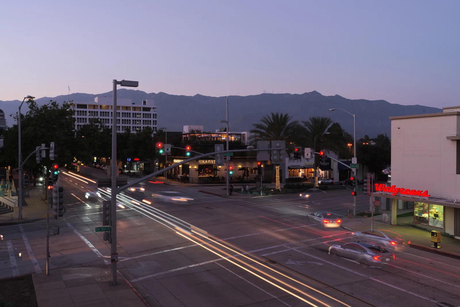 Busy downtown intersection at dusk with traffic signals, car light trails and mountains in the background